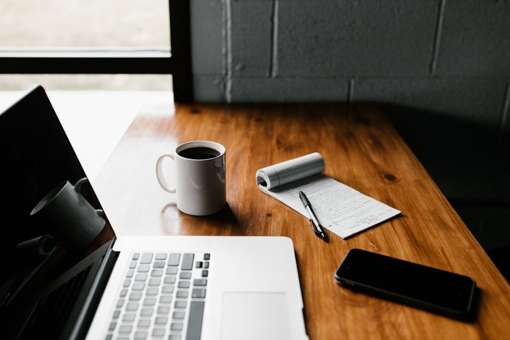 Website-Analyse für redaktionelles SEO:
Ein Arbeitsplatz mit Laptop, Notizblock, Smartphone und einer Tasse schwarzen Kaffee. 